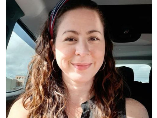 Woman with long hair smiling in a car. Text discusses a case about a failed protection order. Sunny day, wearing black top.