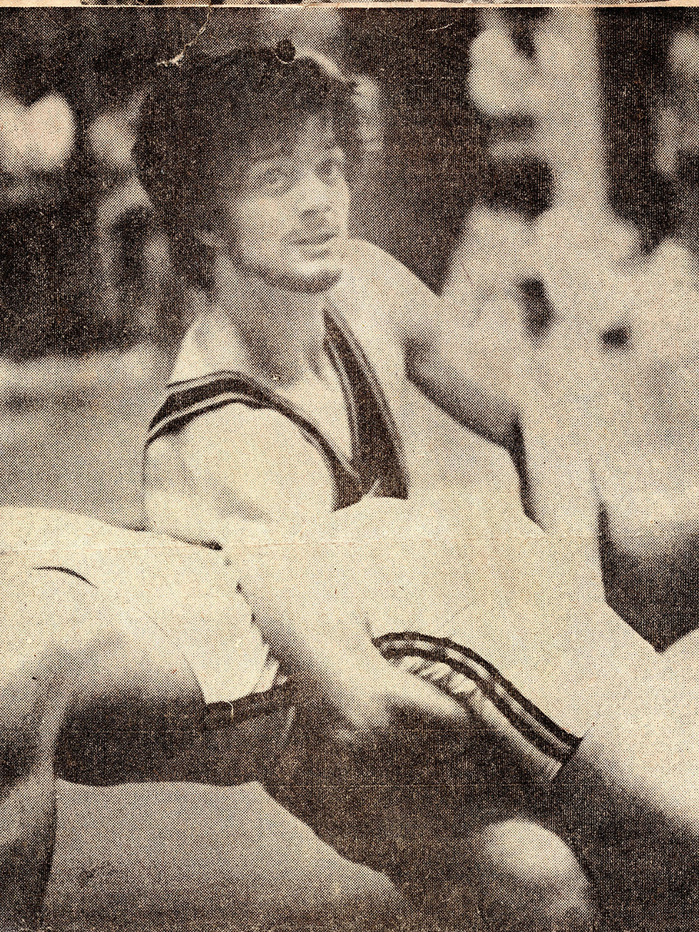 A wrestler in action during a match in a vintage photo. He is gripping an opponent, wearing a striped uniform, with a focused expression.