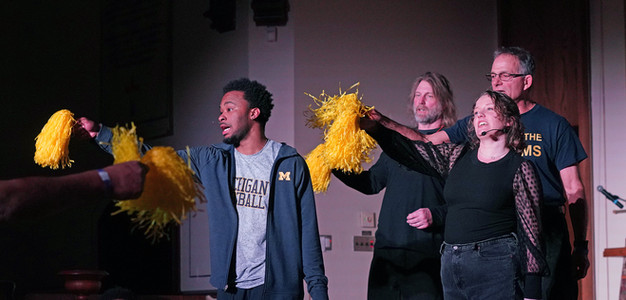 A group of three men and one woman holding yellow pom poms