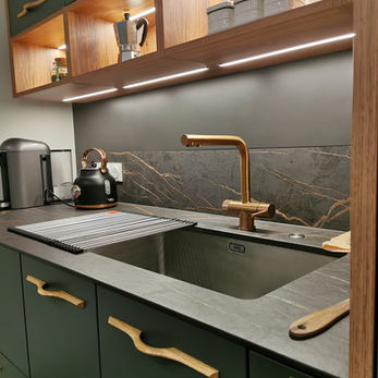 Cette cuisine compacte allie esthétique et fonctionnalité avec ses façades en deux tons et une crédence artistique en Dibon. L’implantation en L, optimisée pour inclure un coin-repas, facilite les déplacements grâce à une disposition en triangle d’activité. Les plans de travail, généreux malgré l'espace réduit, incluent une cuve sous-plan et un égouttoir amovible pour une utilisation flexible. La plaque Bora S Pure, intégrée de manière compacte, assure une cuisson de haute qualité. Les façades en stratifié haute pression avec effet métal et les poignées cuivrées ajoutent une touche élégante, faisant de cette cuisine un exemple parfait de design moderne et pratique.