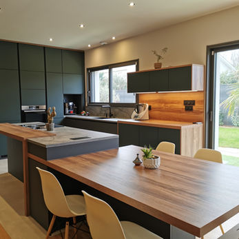 Cette cuisine est un chef-d’œuvre d’aménagement, parfaitement étudiée pour s’intégrer dans une pièce rectangulaire. Elle allie une géométrie précise à une architecture fonctionnelle, combinant un coin repas XXL avec une zone de cuisson intégrée. Le mur d’armoires, organisé en un linéaire épuré, maximise le rangement tout en offrant un design en trois tons soigneusement choisis pour une harmonie visuelle parfaite.