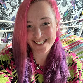 Claire Standen - Close-up selfie of a smiling woman with bright pink and purple hair, wearing a neon green and pink patterned