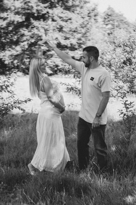 Schwangere Frau und Mann tanzen im Grünen, BABYBAUCH, Natur im Hintergrund.