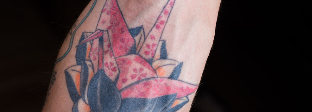 Origami crane and lotus flower tattoo on an arm.