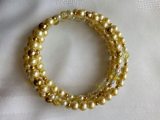 A bracelet made of yellow beads and gold wire site on a white tablecloth.
