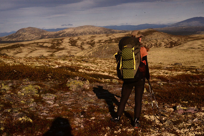 Frau mit Rucksack blickt in die Weite einer nordischen Fjälllandschaft – Symbol für Freiheit und Fernwanderung.