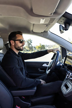 Professional English-speaking driver with beard and sunglasses confidently driving a luxurious Mercedes-Benz V-Class during a long-distance private transfer across Europe, premium and comfortable service by MYEUTAXI