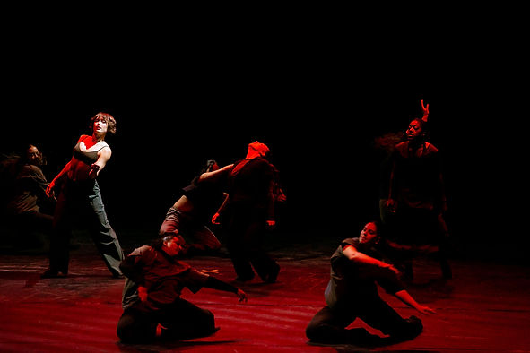Group of dancers performing contemporary dance on stage with red lighting