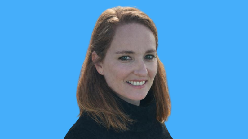 Photo of Marie Kopp – a white woman with reddish brown hair wearing a black turtleneck against a blue background. 
