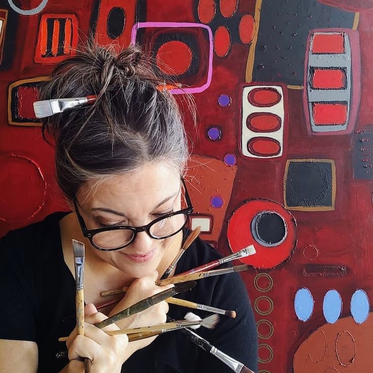 Donna Schwandt with paint brushes in front of vibrant textured painting