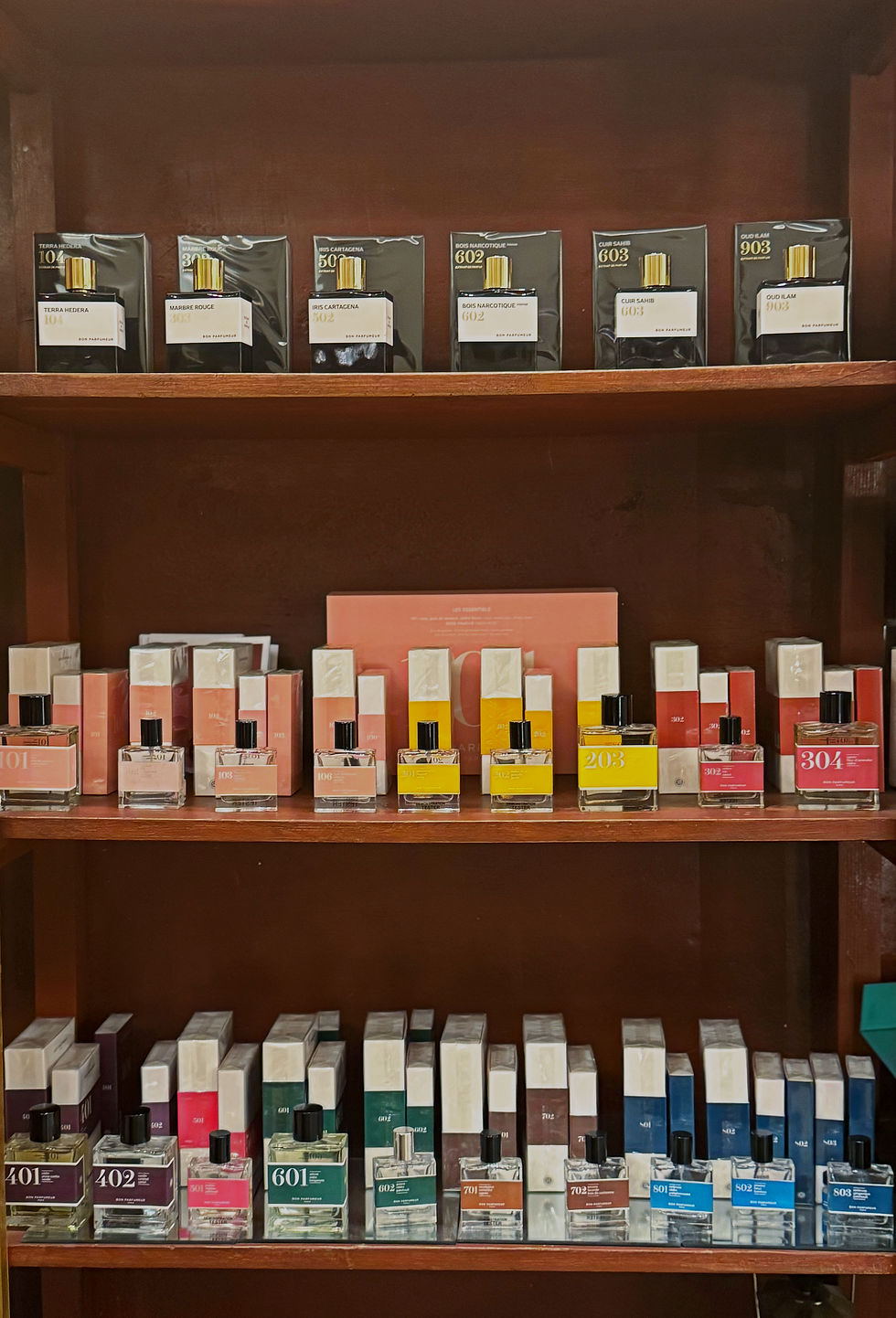 Shelves displaying various colorful perfume bottles and boxes with visible text showing numbers like 104, 203, and 304. Wooden background.