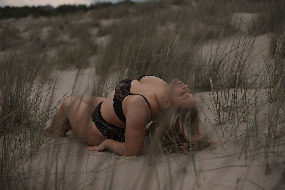 A boudoir photograph taken by photographer Pauliina Tähkäpää shows a blonde woman lying on the beach wearing black lace underwear