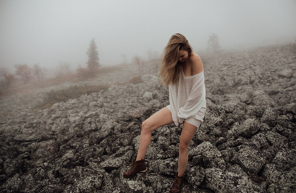 Pitkätukkainen, vaalea nainen seisoo keskellä harmaata ja sumuista pirunpeltoa Levitunturin huipulla boudoir kuvassa. Naisellä on päällä valkoinen, löysä ja iso neule, joka peittää naisen vartalon olkapäältä reisiin asti. Naisen etureidet ja sääret ovat paljaat. Naisella on jalassaan tummat vaelluskengät ja hänen toinen jalka on koukussa vartalon edessä. Naiset kädet ovat päällekkäin naisen lantion kohdalla. Nainen katsoo pois päin valokuvaajasta kohti käsiään. Naisen hiukset ovat rennosti tuulen sekoittamat ja peittävät osittain naisen kasvot. Nainen nauraa ja näyttää huvittuneelta seistessään syksyllä keskellä Levitunturia keskellä sumua.