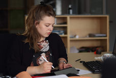 eine junge attraktive Frau bedient mit einem Pen ein Grafiktablet an einem Schreibtisch