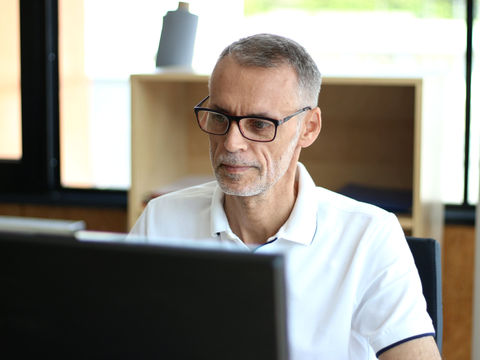 ein Mann mit grauem Haar und Brille sieht in einen PC-Bildschirm