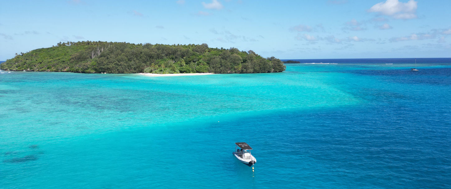 Small boat in clear turquoise ocean water near lush green island.