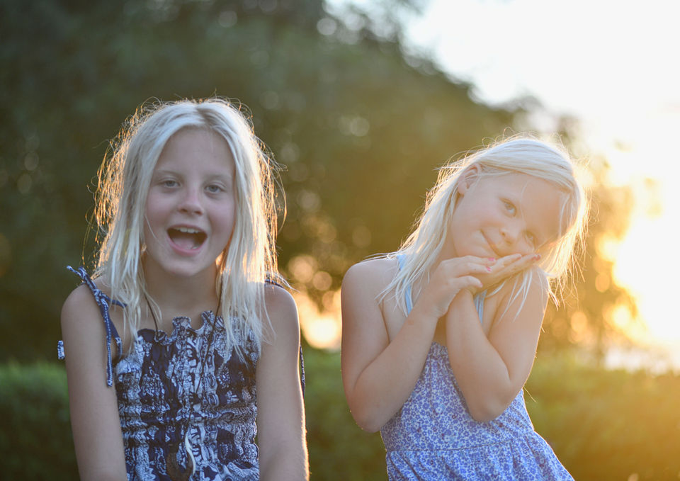 Two young girls smiling outdoors, enjoying the sunlight in a summer field.