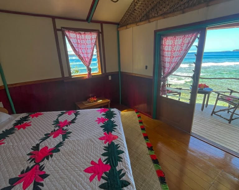 Cozy bedroom with colorful bedspread, open door leading to ocean view.