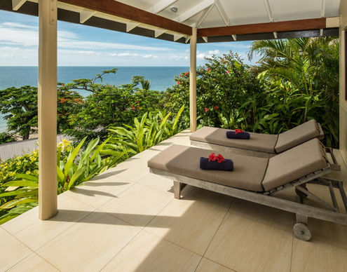 Two lounge chairs on a patio overlooking the ocean and lush greenery.