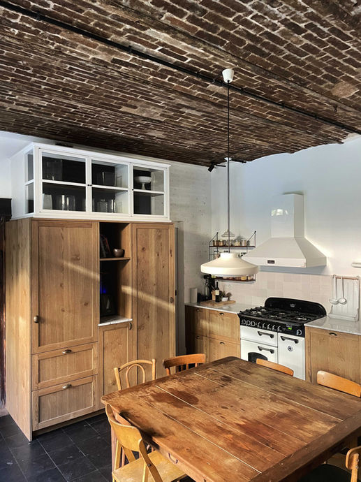 alt="le mélange des meubles en bois brut, de la brique au plafond, et du blanc confère à cette cuisine située dans une maison au cœur de Paris un air de campagne vintage"