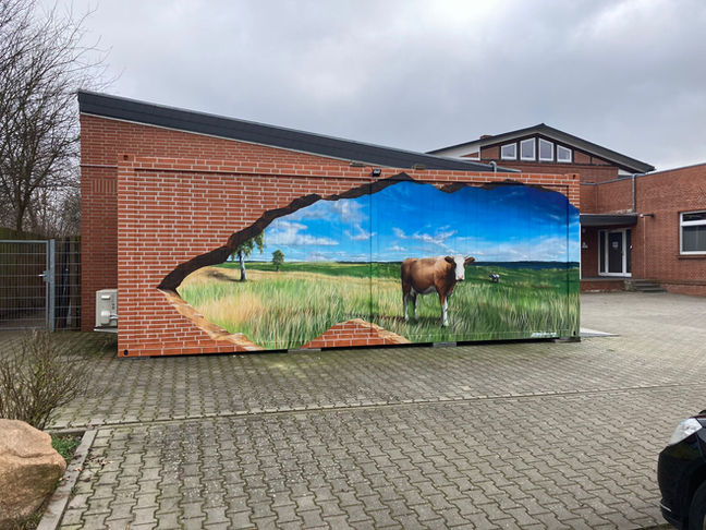 Farbenfrohes Streetart Gemälde auf Backsteingebäude  mit einer Kuh in einer ländlichen Landschaft