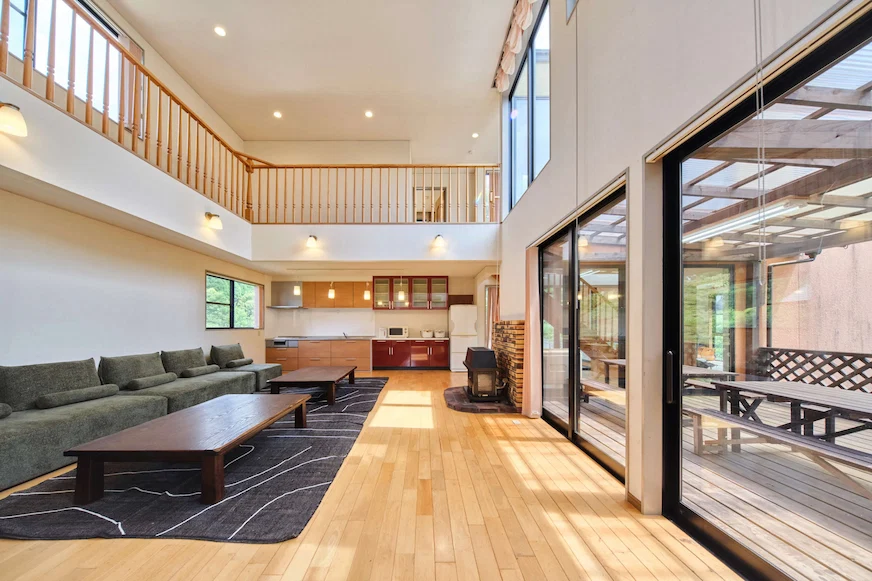 寬敞的客廳,木地板,大窗戶採光好。灰色沙發和長木桌,牆上有簡單燈具。廚房開放,現代感十足