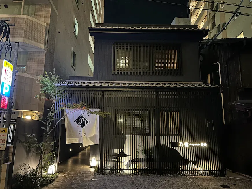 夜間街景中,一座黑色傳統日式建築,前有白色布幔,上寫