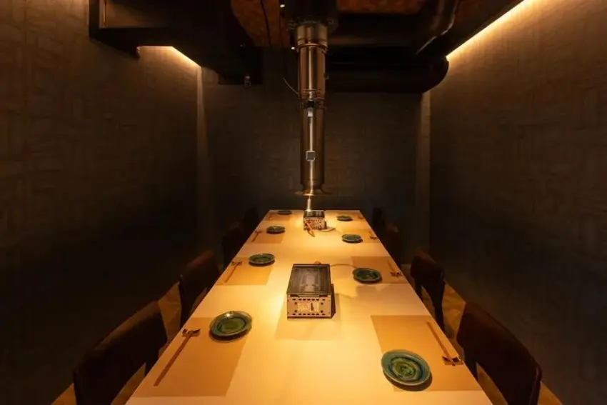 昏暗的私人餐廳內,一張長桌整齊擺著餐盤和餐具,中央有懸掛裝置,氛圍安靜神秘