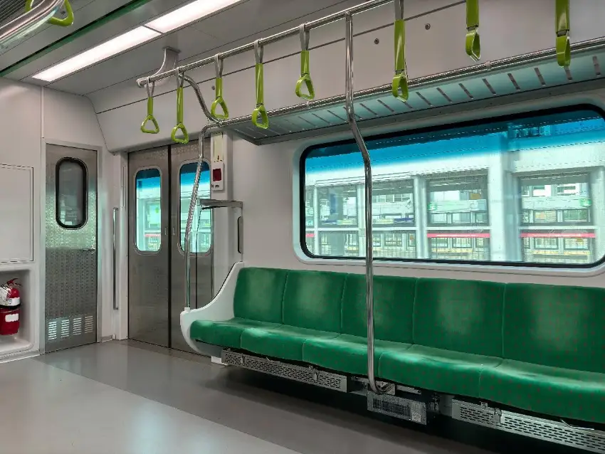 空蕩的地鐵車廂內,綠色長座椅和吊環整齊排列,窗外可見月台與建築,環境明亮整潔,安靜無人