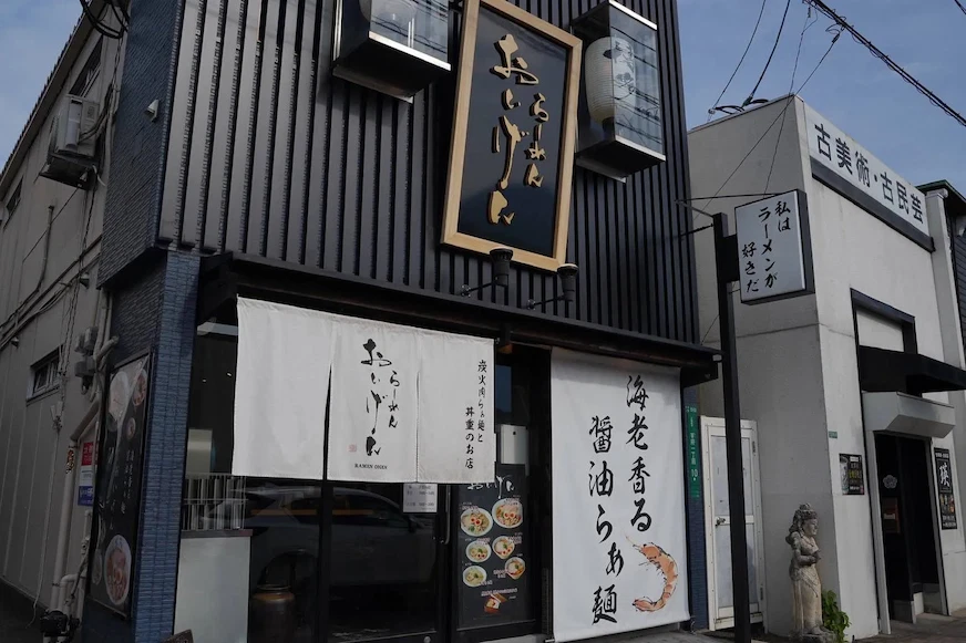 黑色外牆餐廳,掛有白色門簾,上印日文,展示海鮮菜色。右側建築上寫著「古美術、古民芸」。氛圍寧靜