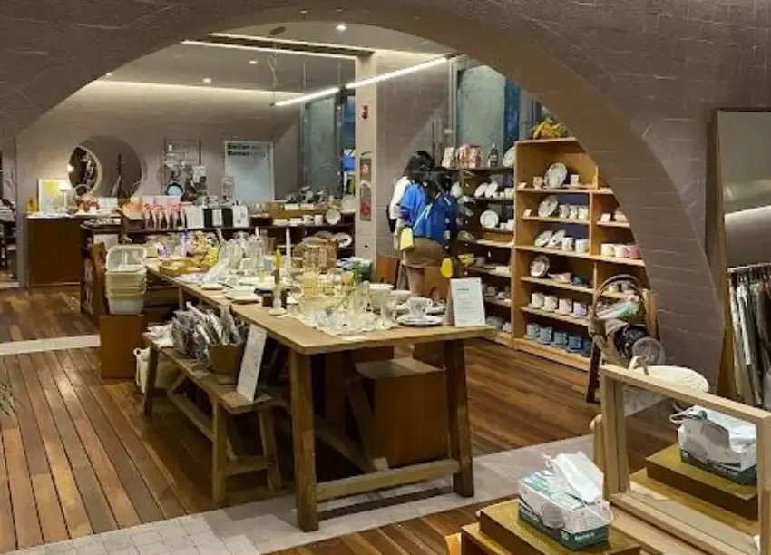 溫暖燈光下的家居店內景,木桌上陳列玻璃杯、餐具和小擺件,右側貨架擺滿餐盤與杯子,氛圍安靜整潔