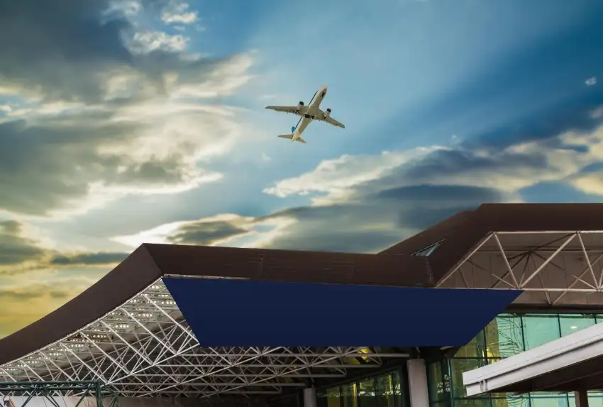 一架客機飛過現代機場建築上空,天空藍金相間、雲層厚重,畫面開闊寧靜
