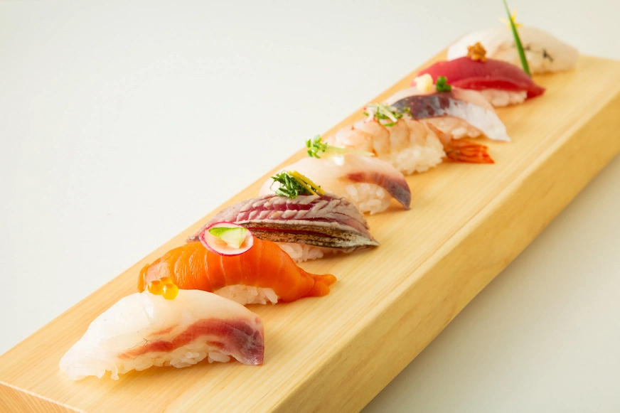 木托盤上整齊擺放著七塊不同種類的壽司,顏色鮮豔,背景簡單,給人一種優雅精緻的感覺