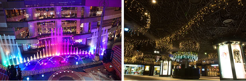 室內購物中心的噴泉展現出彩虹色光芒,旁邊天花板掛滿閃爍燈飾,環境明亮且充滿節日氣氛