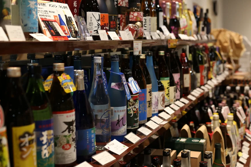 貨架上排列著各種酒瓶,背景模糊。酒瓶色彩豐富,標籤上文字清晰可見,營造出琳瑯滿目的視覺效果