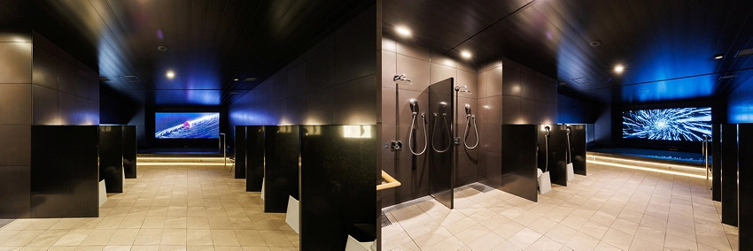 現代淋浴間,黑色牆壁與瓷磚地板。背景有大螢幕顯示海洋與抽象圖案。環境燈光昏暗,氣氛安靜