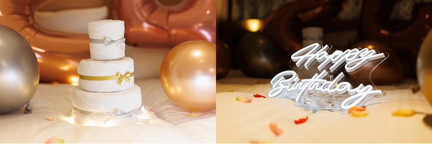 床上放著毛巾蛋糕和氣球,背景有「Happy Birthday」燈飾,色彩柔和,營造出慶祝生日的溫馨氛圍