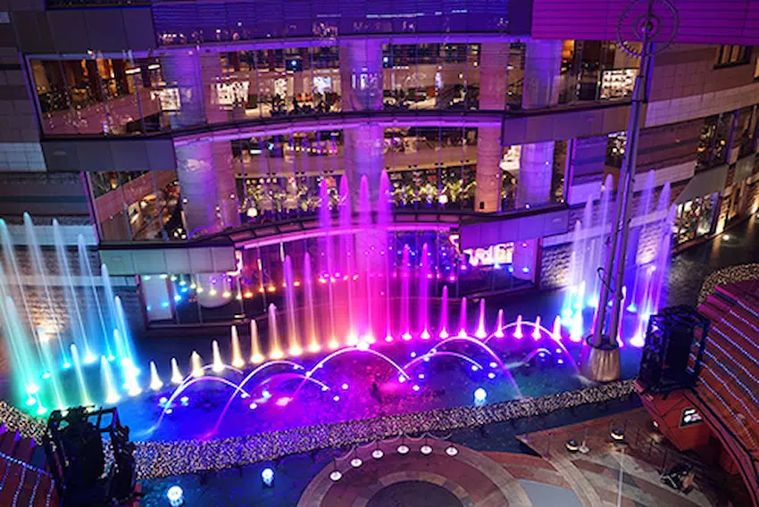 彩虹燈光下的噴泉在夜晚的商場中展現,背景是明亮的玻璃窗,氣氛充滿活力與現代感