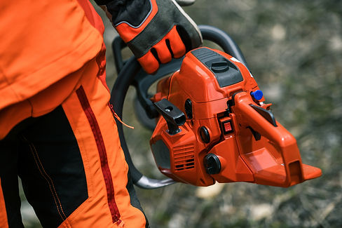 Close up view of an hand holding a chainsaw. Lumberjack at work wears orange personal prot