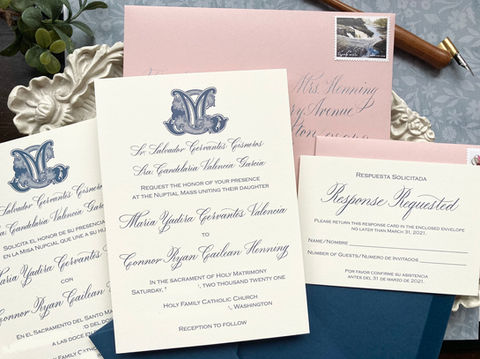 Cream-colored wedding invitation with navy blue calligraphy, a vintage style duogram of the couple's initials, and dusty pink envelopes