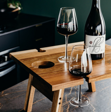 Folding wine table with bottle of red wine and 2 long stemmed glasses.