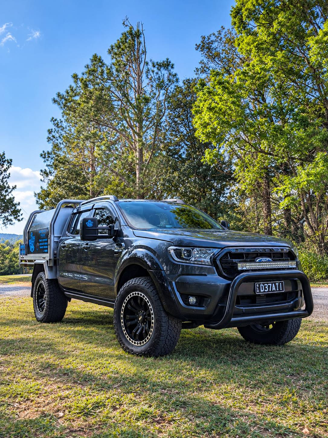 Jesse's dark grey Ford Ranger double cab with a silver tray and blue Crystallize signage, parked on grass under blue sky