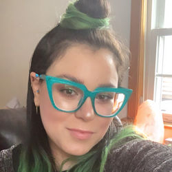 girl with long brown/green hair and a top knot with green glasses is smiling