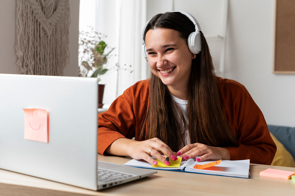 Smiling woman with headphones at a desk, writing on sticky notes. Laptop with smiley sticker, cozy room with plants and macramé decor.