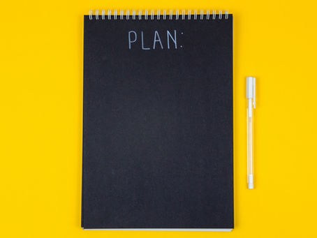 A black notebook with "PLAN:" at the top and a white pen beside it on a bright yellow background, creating a vibrant and organized mood.