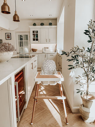 black and white cushion cover on a ikea antilop highchair with cover baby accessories, inclusing a pink placemat for the tray and bamboo leg stickers and a bamboo footrest in a modern cream coloured kitchen with an olive tree on the right