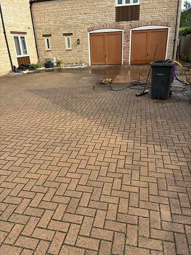 Block paving driveway before and after pressure washing, split by a dashed line