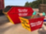 Two large, bright red skip bins with yellow accents are parked on a construction site