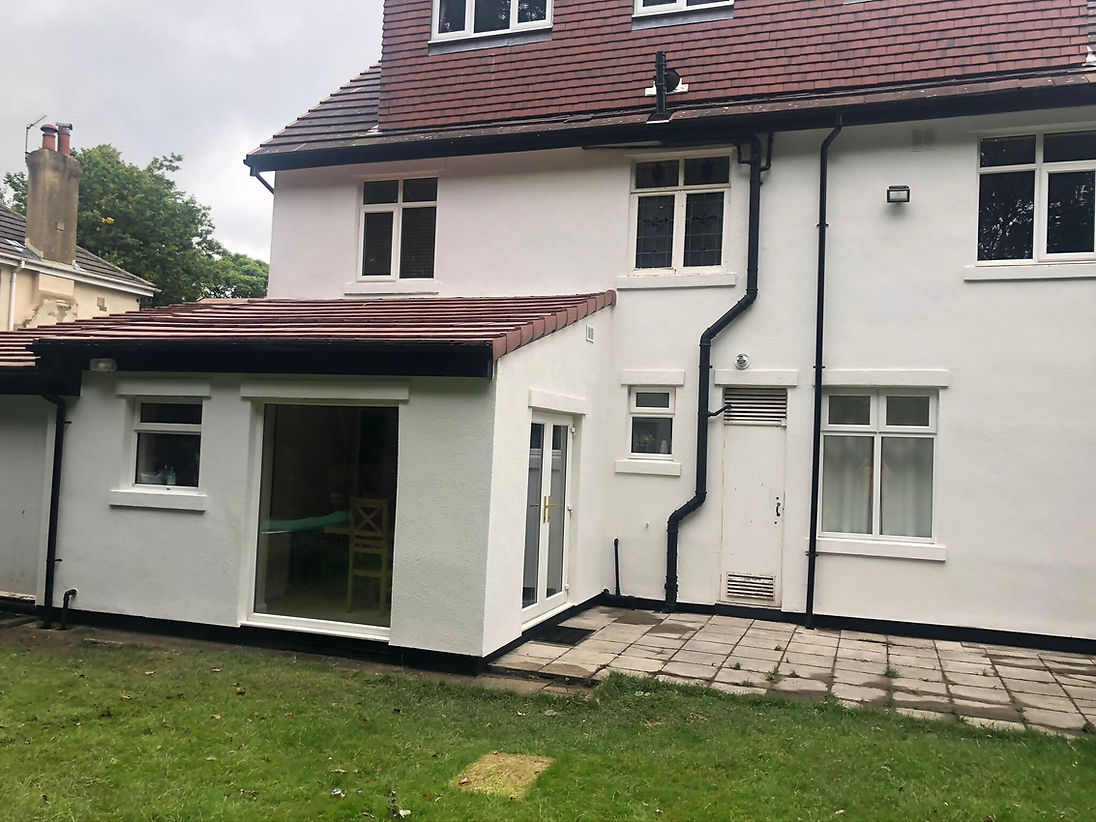 A white two-story house with a red-tiled roof and rectangular extension, featuring large windows and a small patio