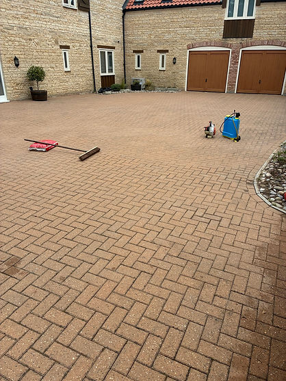 Before-and-after comparison of a brick paver driveway with cleaning equipment nearby